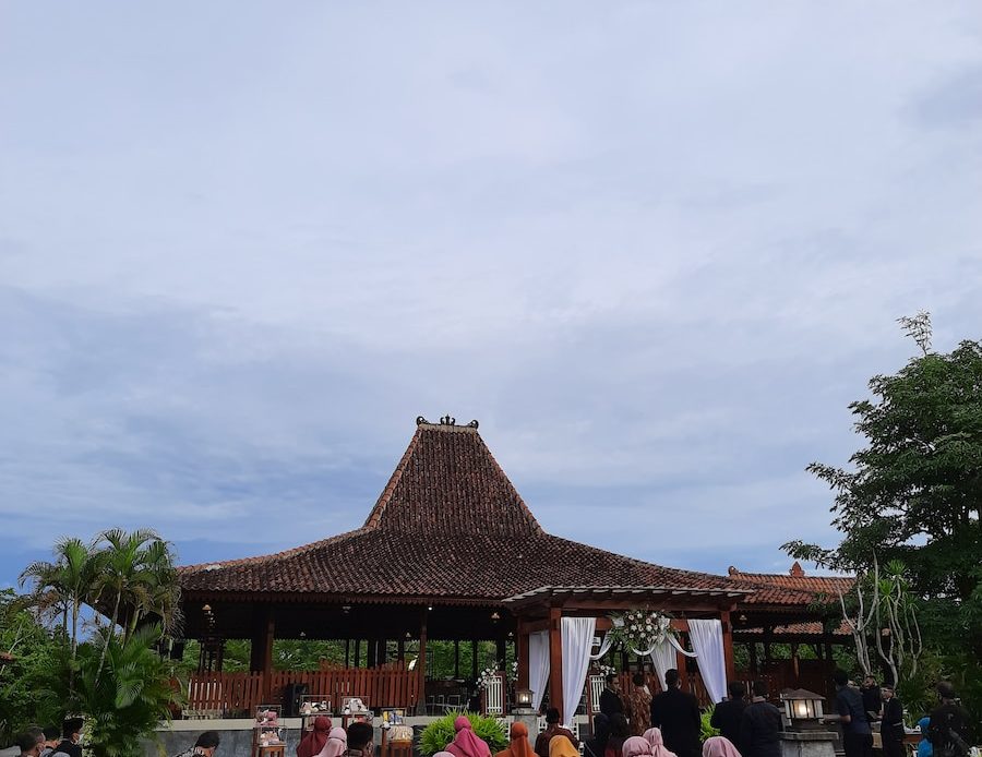 people sitting on chairs near brown wooden house under white clouds during daytime
