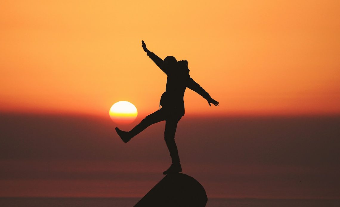 photo of silhouette photo of man standing on rock