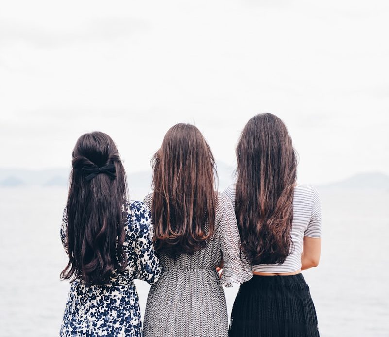 three woman looking back and facing body of water