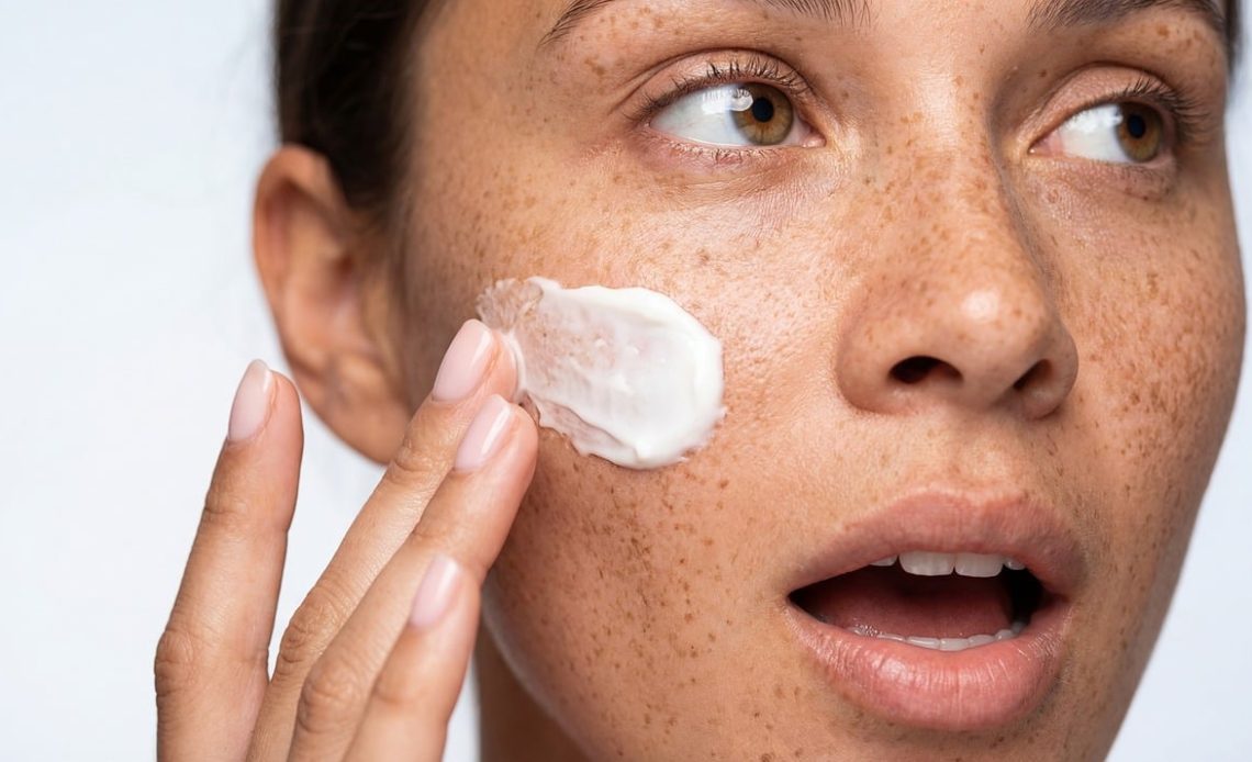 Vrouw die huidverzorgingsproducten voor acne-gevoelige huid gebruikt aan haar wastafel