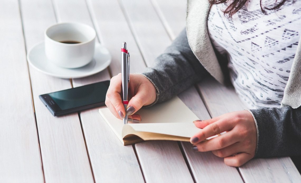 Een vrouw schrijft in een notitieboekje aan haar bureau, verzonken in gedachten